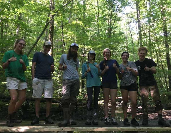 7 sustainability people- staff and students- stand lined up on a boardwalk they just repaired with thumbs up